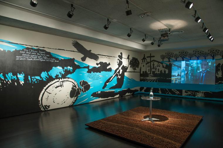 Black-and-white mural of historic Santa Clara imagery with an acorn rug in the middle of the room.