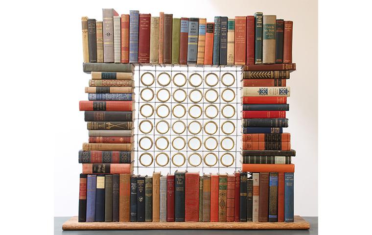 Sculpture created by books arranged in open square with glass lenses in the center