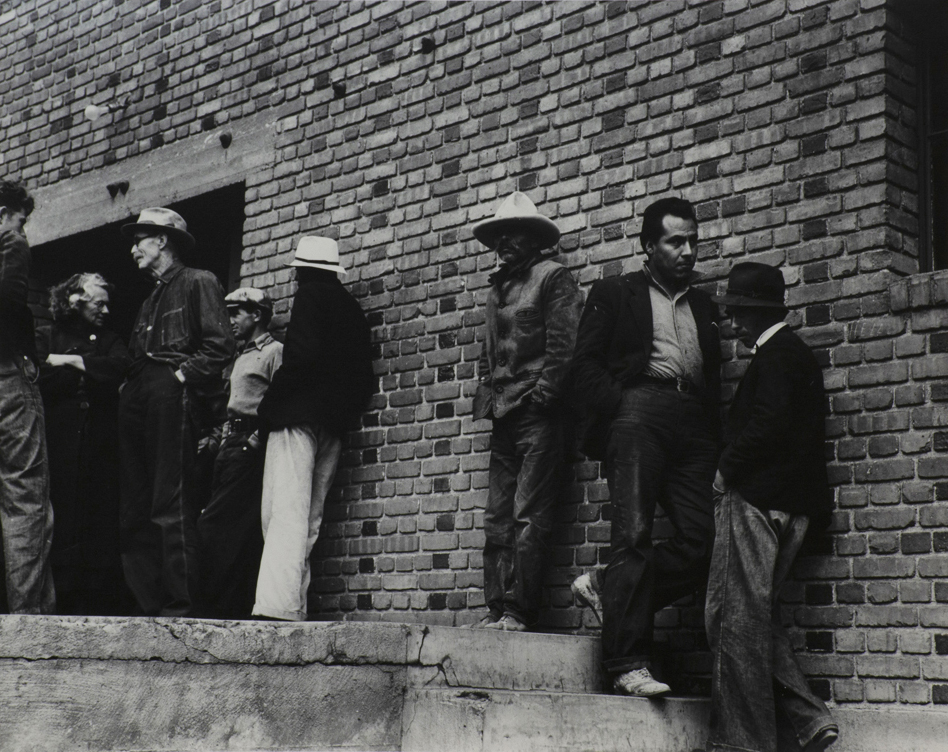 Black and white photograph of eight laborers on strike standing outside of brick building.
