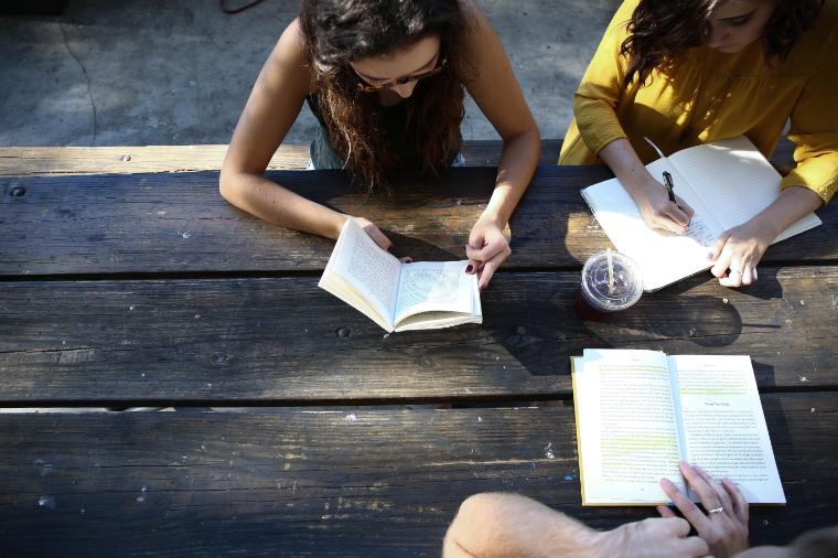 Alt text: Students discussing notes while seated at a wooden table outdoors.