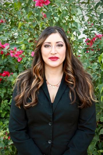 A woman in black attire standing in front of a plant with red flowers.