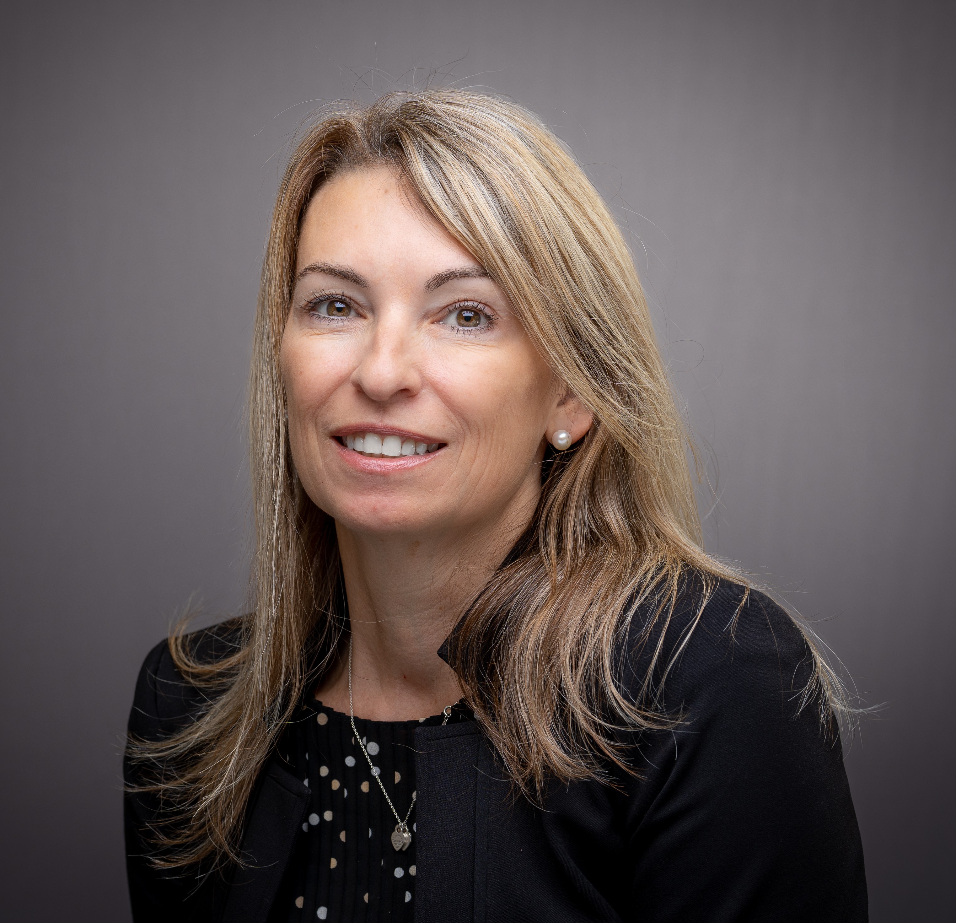 A person with a neutral expression against a gray background.