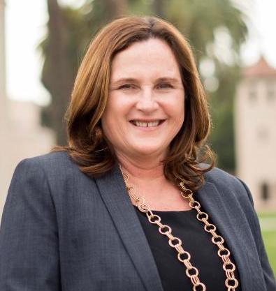 A woman in professional attire smiling outdoors near a building.