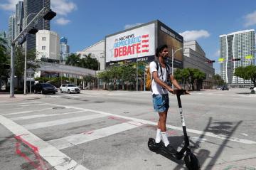 A person rides a scooter near a Democratic presidential debate banner. image link to story