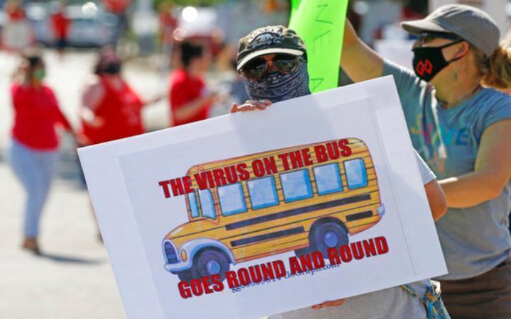 a person wearing facemask and carrying a sign with an image of a school bus and slogal 
