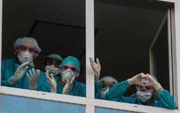medical staff wearing face masks and scrubs wave and send heart messages from window