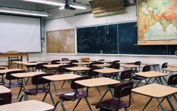 an empty classroom with rows of desks, chalkboards, and maps