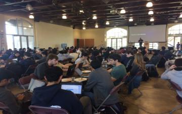 students at tables with computers participating in hackathon