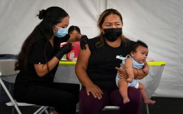 Laura Sanchez, right, holds her 2-month-old son, Lizandro, while receiving a dose of the Pfizer COVID-19 vaccine from a registered nurse, Noleen Nobleza at a vaccine clinic set up in the parking lot of CalOptima in Orange, Calif. Gov. Gavin Newsom announced Tuesday, Aug. 31, 2021 that more than 80% of the people eligible to receive the coronavirus vaccine in CA