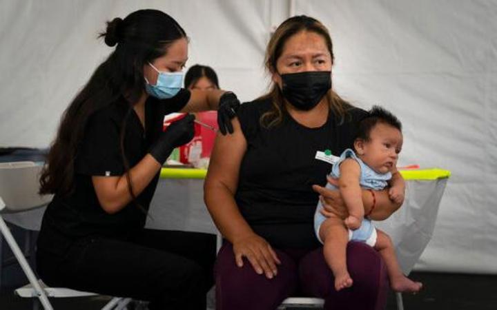 Laura Sanchez, right, holds her 2-month-old son, Lizandro, while receiving a dose of the Pfizer COVID-19 vaccine from a registered nurse, Noleen Nobleza at a vaccine clinic set up in the parking lot of CalOptima in Orange, Calif. Gov. Gavin Newsom announced Tuesday, Aug. 31, 2021 that more than 80% of the people eligible to receive the coronavirus vaccine in CA