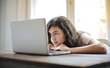 student sitting in front of laptop computer resting her head in hands