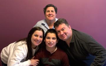 Four people smiling in front of a purple wall.