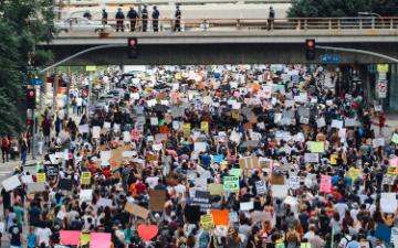 A large group of people gathered, holding protest signs on a city street.