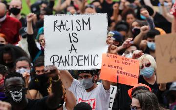 protester in crowd holding sign that says Racism is a Pandemic