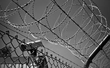 barbed wire across the top of a chain linked fence with security tower in background