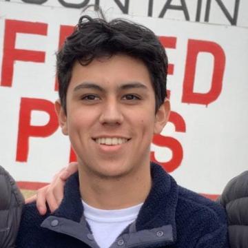 A smiling person in front of a sign with partial text.