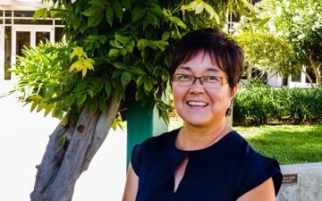 A person named Naomi smiling outdoors near trees.