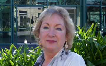 A woman stands in front of green foliage and buildings.