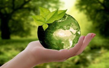 A hand holding a clear sphere with a leaf on it.