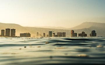 Trash in body of water with a cityscape in the background.