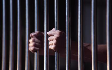 Two hands holding bars in a jail cell. Photo by sakhorn_Adobe Stock. 