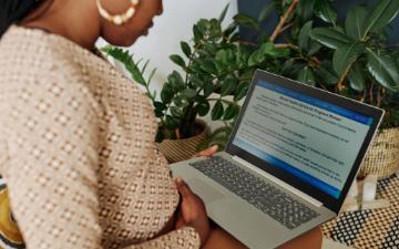 A pregnant Black woman sitting with laptop and reading about pregnancy online. By AnnaStills_Adobe Stock