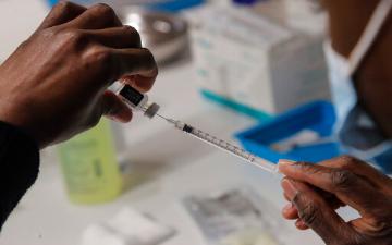 Two hands preparing Pfizer COVID-19 vaccine with syringe. 