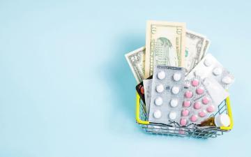 A shopping basket filled with pills and money. Photo by Anastasiia Gudantova on Unsplash.