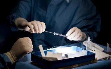 A person handling lab equipment and a syringe with focus on a petri dish.