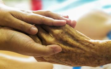 An elderly patients hand being held by a caregiver