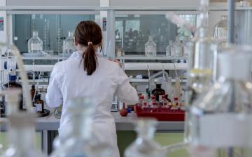 A doctor in a laboratory facing equipment and glassware.