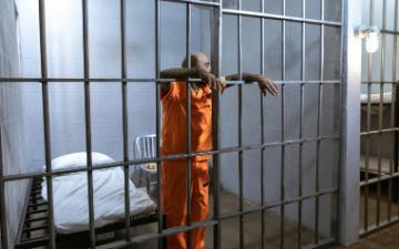 Man in orange uniform standing beside gray metal gate. Photo by RDNE Stock project/Pexels