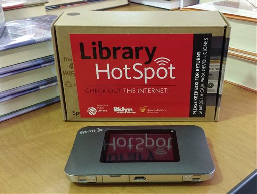 Library lending hotspot sign and hotspot device on a table. Books are in the background.