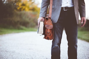 Image of a man wearing a leather briefcase and holding a book. 