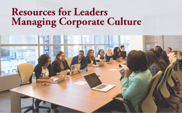 A business meeting with diverse group of participants sitting at a conference table with laptops and notebooks engaging in a conversation 