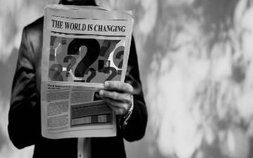 man wearing business suit holding a newspaper with world is changing headline