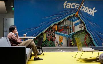 A person sitting in a room with a Facebook-themed wall mural. image link to story