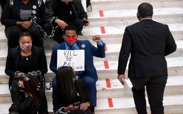 Person holding a protest sign reading End Voter Suppression while sitting on steps. image link to story