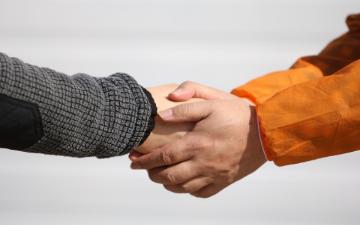 Two hands hold another hand in embrace