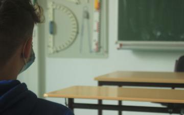 student wearing face mask sitting in empty classroom