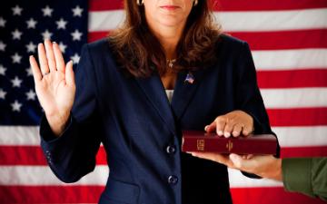 Person taking an oath with hand raised and holding a book. image link to story