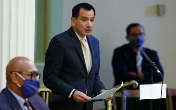 A man speaks at a podium while two other men listen. image link to story
