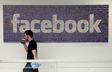 Man walking past a wall with a large Facebook logo. image link to story