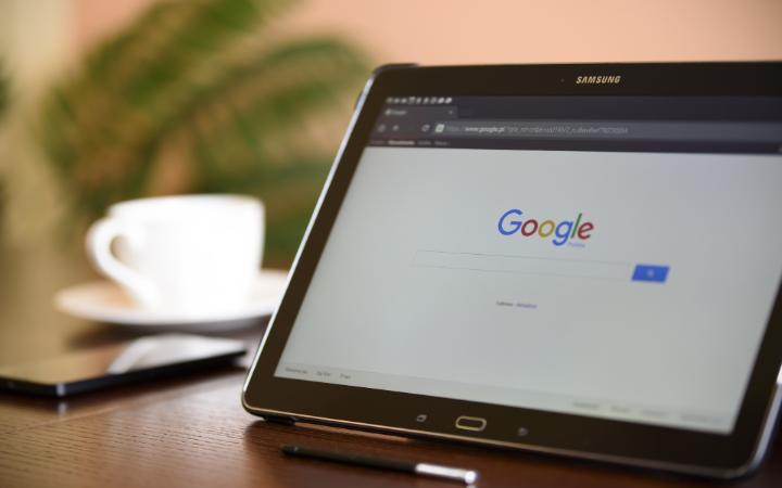 Tablet displaying Google search engine on screen, next to a cup and laptop. image link to story