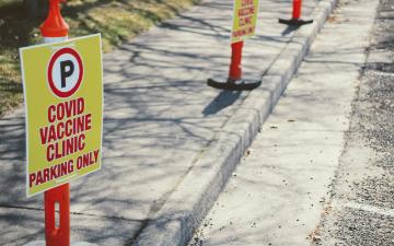 COVID vaccine sign reading NO PARKING COVID LINE ENTER HERE near walkway. image link to story