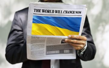 A person holding a newspaper with a large Ukrainian flag on the front page. image link to story