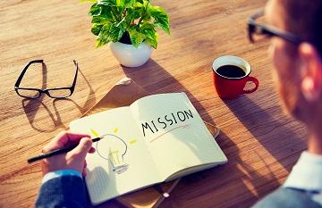 A person writing Mission/Idea in a notebook with a coffee cup nearby. image link to story