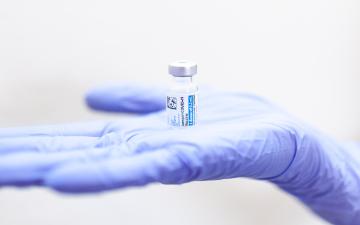 A gloved hand holding a vial labeled J&J COVID-19 Vaccine. image link to story