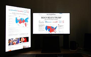 Two monitors displaying voting-related content in a dark room. image link to story