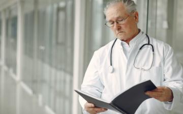 A doctor with a stethoscope reviews notes in a folder. image link to story